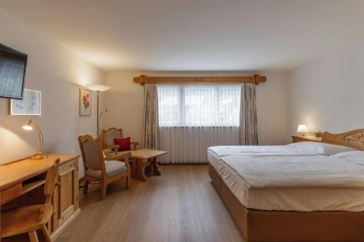 A hotel room with a bed, a desk, a chair, a television, and a window with curtains.