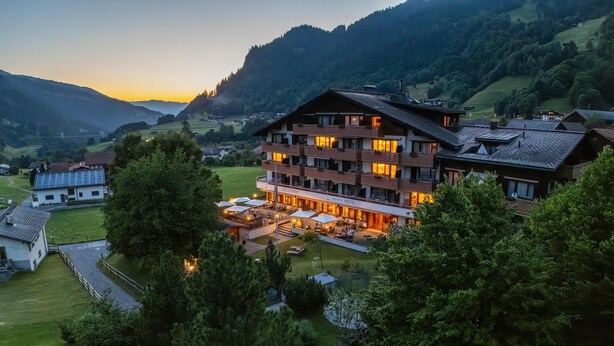 Un hôtel à plusieurs étages doté d’un restaurant et d’un espace extérieur aménagé, entouré d’une végétation luxuriante et de montagnes.