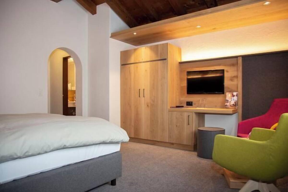 A bedroom with a bed, a wooden wardrobe, a desk with a television, and a red chair.