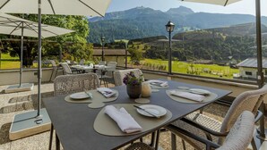 Une terrasse avec des tables et des chaises, un vase rempli de fleurs et une vue sur les montagnes.