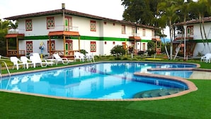 Un'area piscina con diverse piscine, poltrona a sdraio bianche e un edificio con dettagli rossi e verdi.