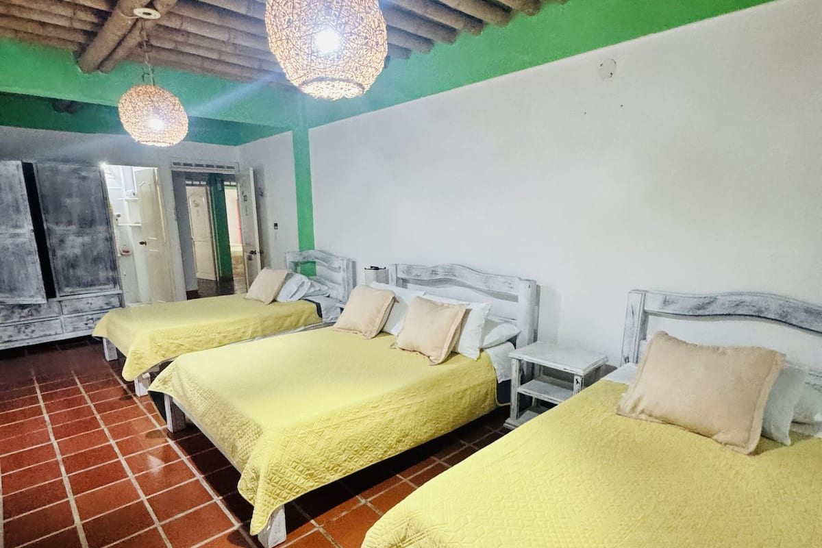 A hotel room with three beds, each with a yellow bedspread and white headboards.