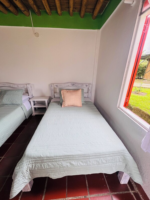 A small, single-room accommodation with a bed, a nightstand, and a window with a view of the outdoors. - Eco Hotel Santa Bárbara (Circasia)
