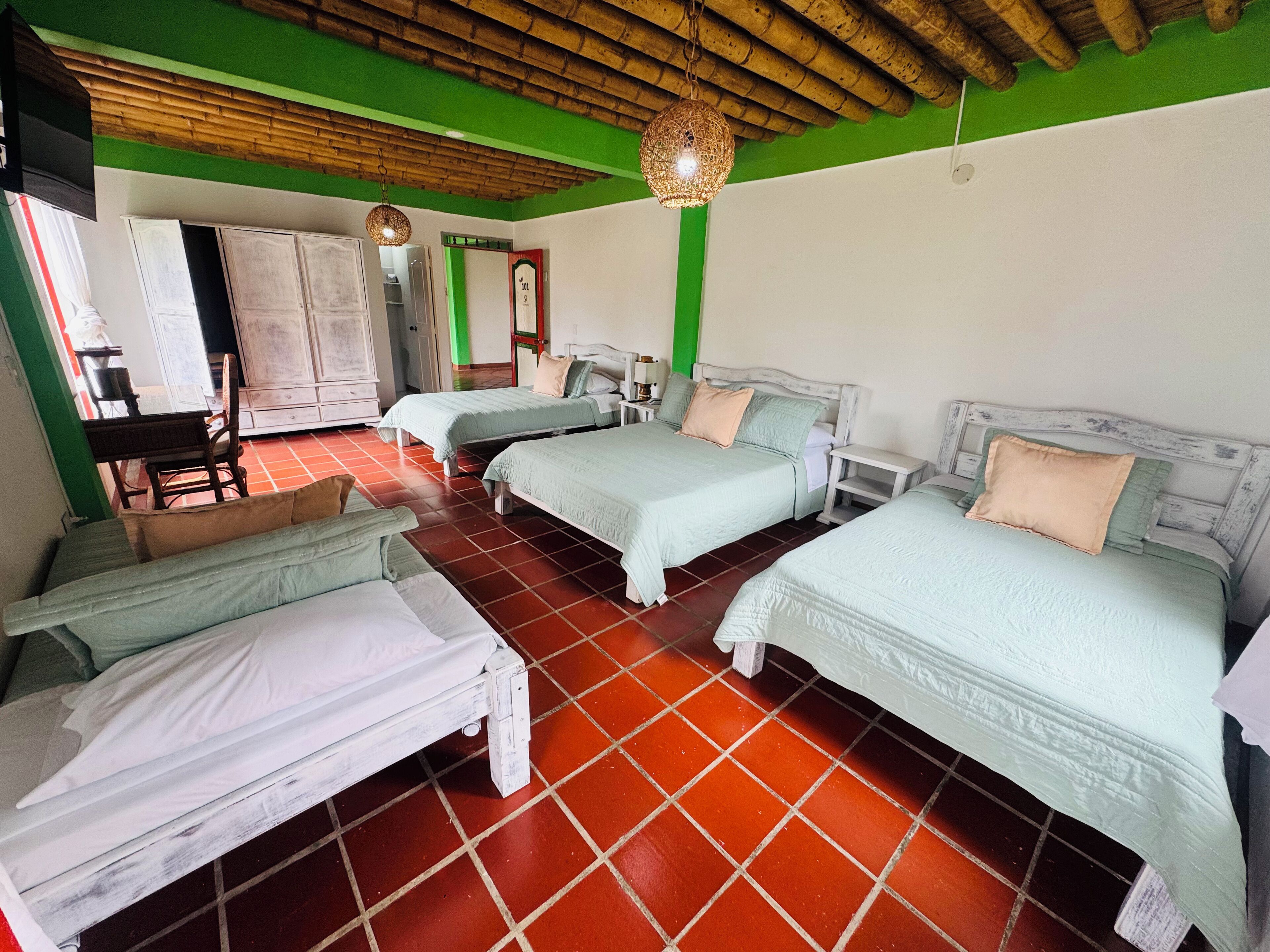 A hotel room with three beds, a dining area, and a kitchen.