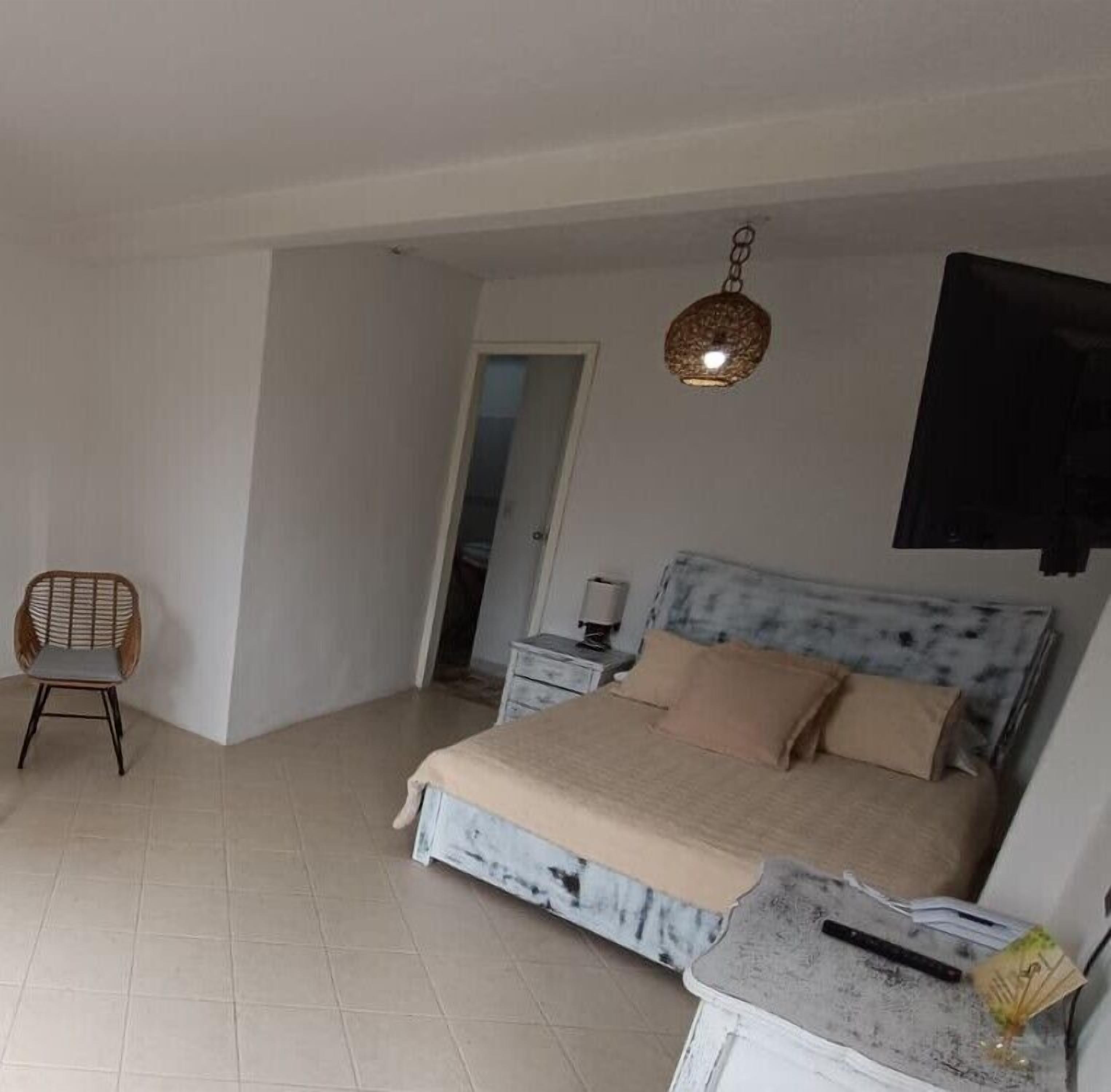 Ein Schlafzimmer mit einem Bett, einem Sessel, einem Nachttisch und einem an der Wand befestigten Fernseher.