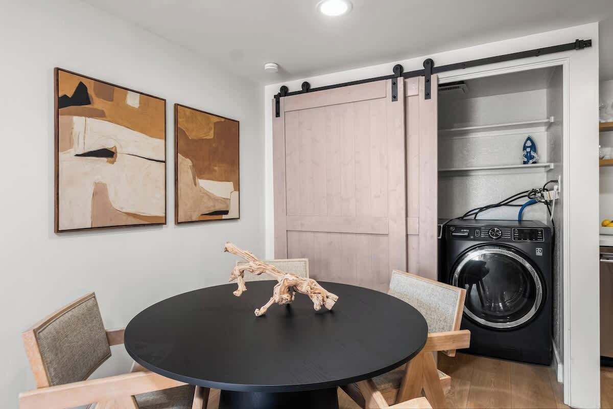 A compact kitchen with a washing machine, a sliding door, and two abstract paintings on the wall.