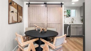 Un comedor con una mesa redonda y cuatro sillas, una puerta corredera estilo granja, y una cocina al fondo.