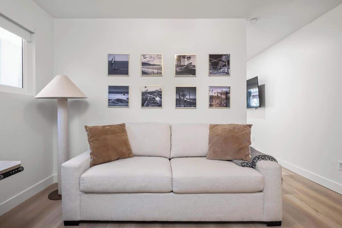 Ein modernes Wohnzimmer mit einem hellen Sofa, einer Stehlampe und einem an der Wand befestigten Flachbildfernseher.