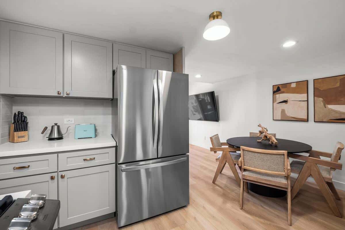 A modern kitchen with stainless steel appliances, white cabinetry, and a dining area with wooden chairs and a black table.