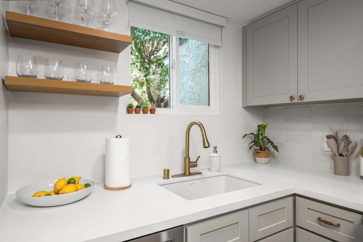 A modern kitchen with white cabinets, a sink, and a window with potted plants.