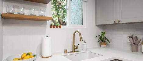 A modern kitchen with white cabinets, a sink, and a window with potted plants.