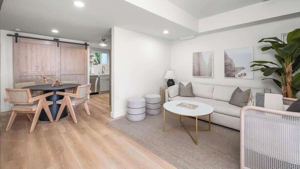 Una sala de estar moderna con comedor, paredes blancas y una planta grande.