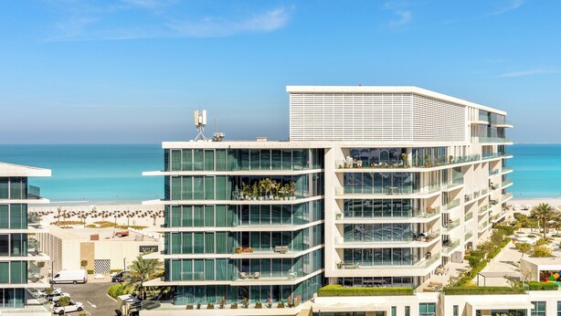 Un hôtel moderne à plusieurs étages, doté de grandes fenêtres et de balcons donnant sur une plage.