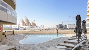 Un espace piscine aménagé sur le toit, avec des chaises longues et une vue sur un bâtiment moderne à l’architecture originale.