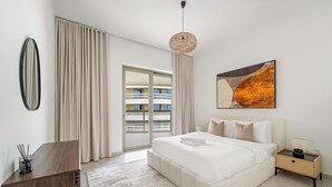 Une chambre moderne avec un grand lit, un bureau en bois, une grande fenêtre avec des rideaux, un luminaire au plafond et un tableau accroché au mur.
