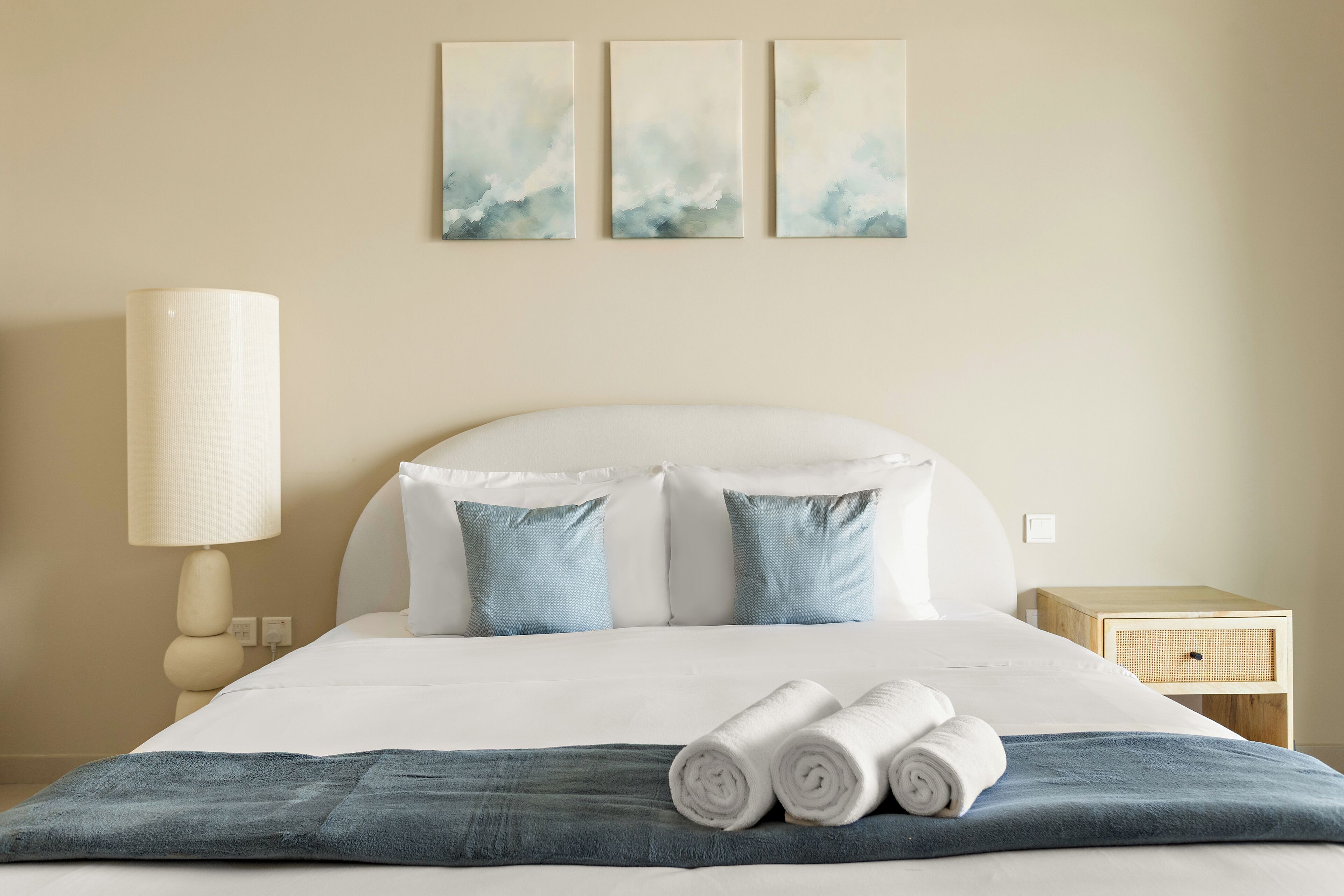 A neatly made bed with pillows, a lamp, and a nightstand with a basket.