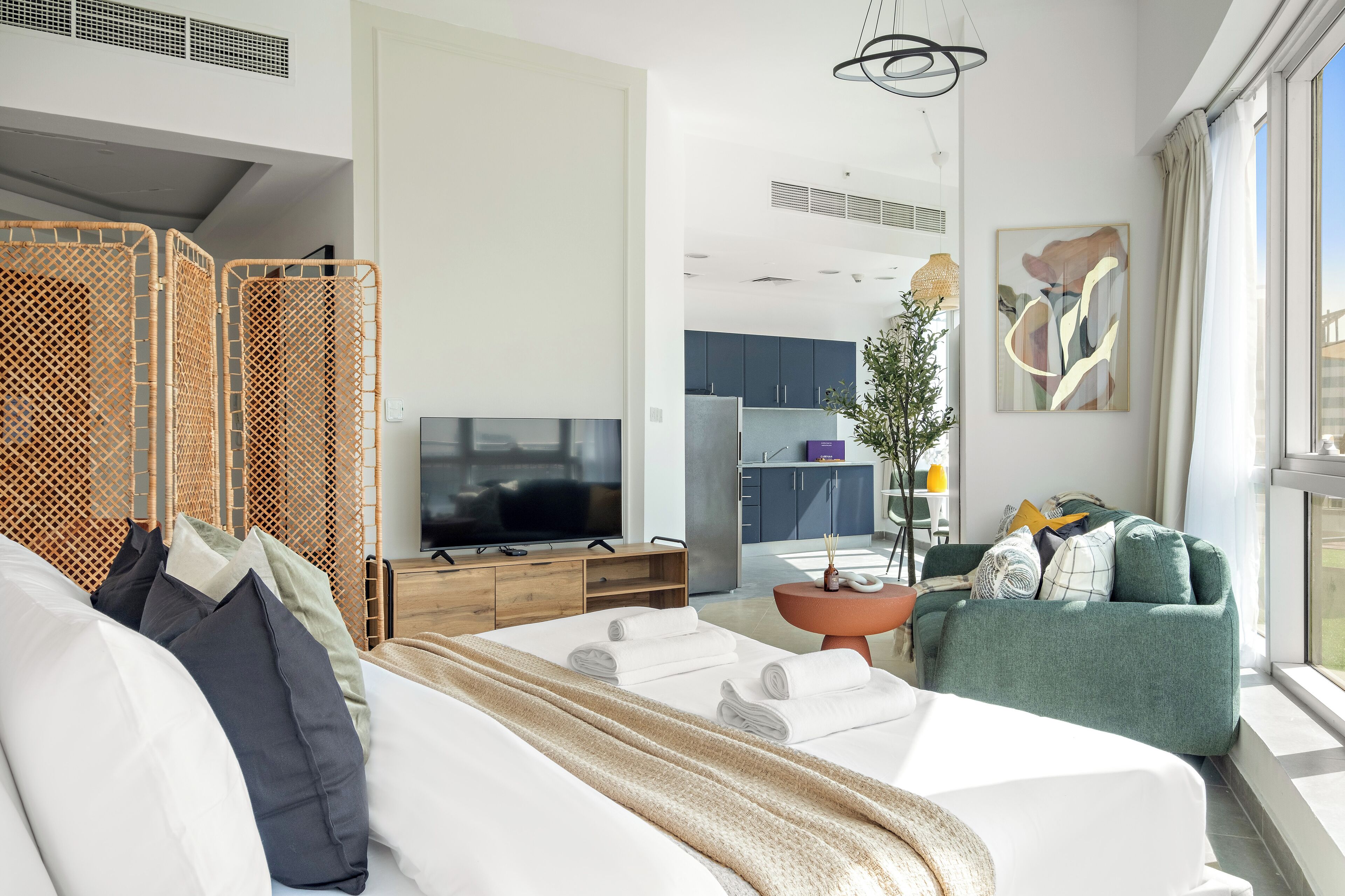 A modern hotel room with a large bed, a television, a dining area, and a view of the outdoors.