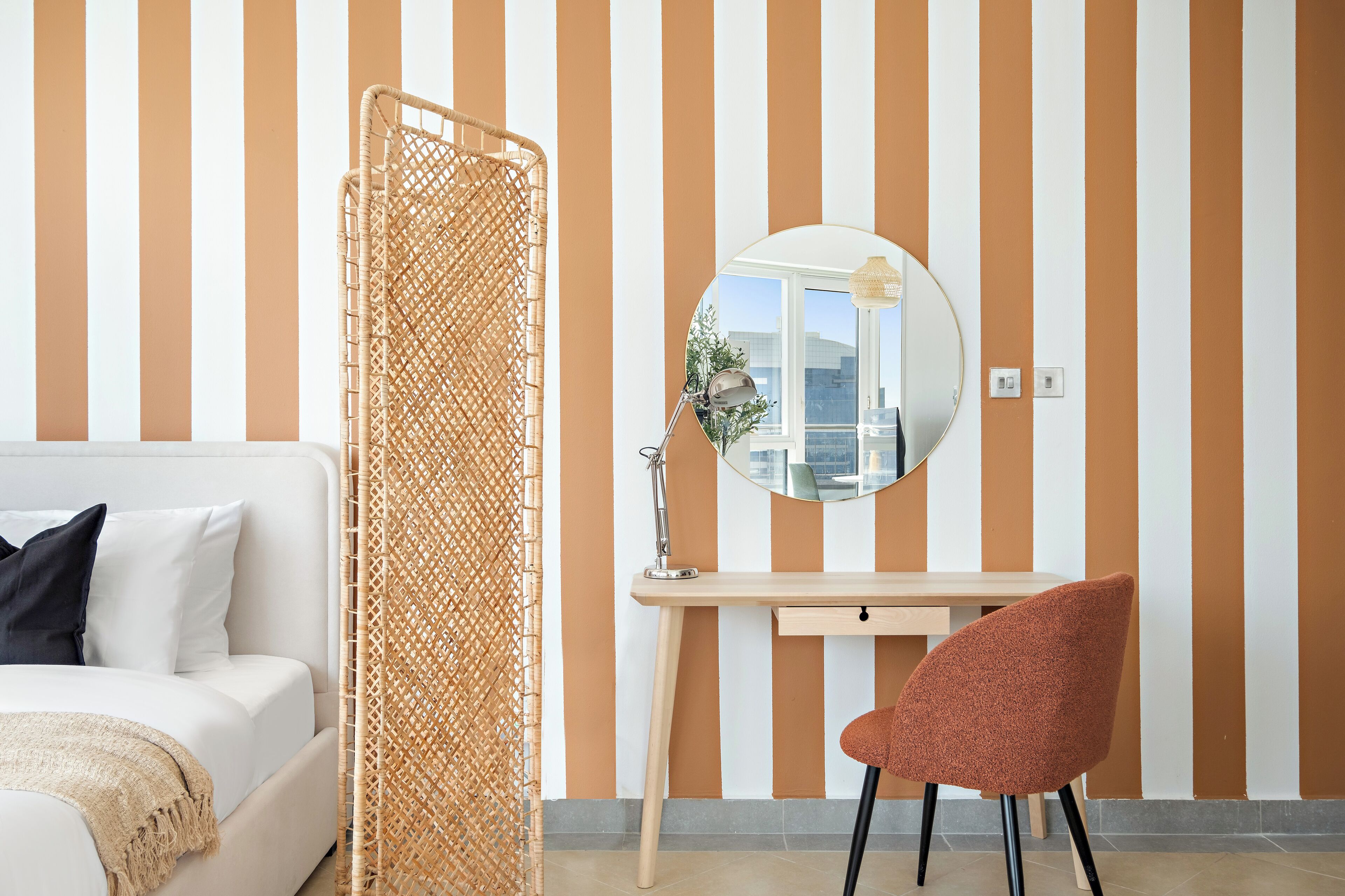 Una habitación con cama, escritorio, silla, espejo y pared a rayas.