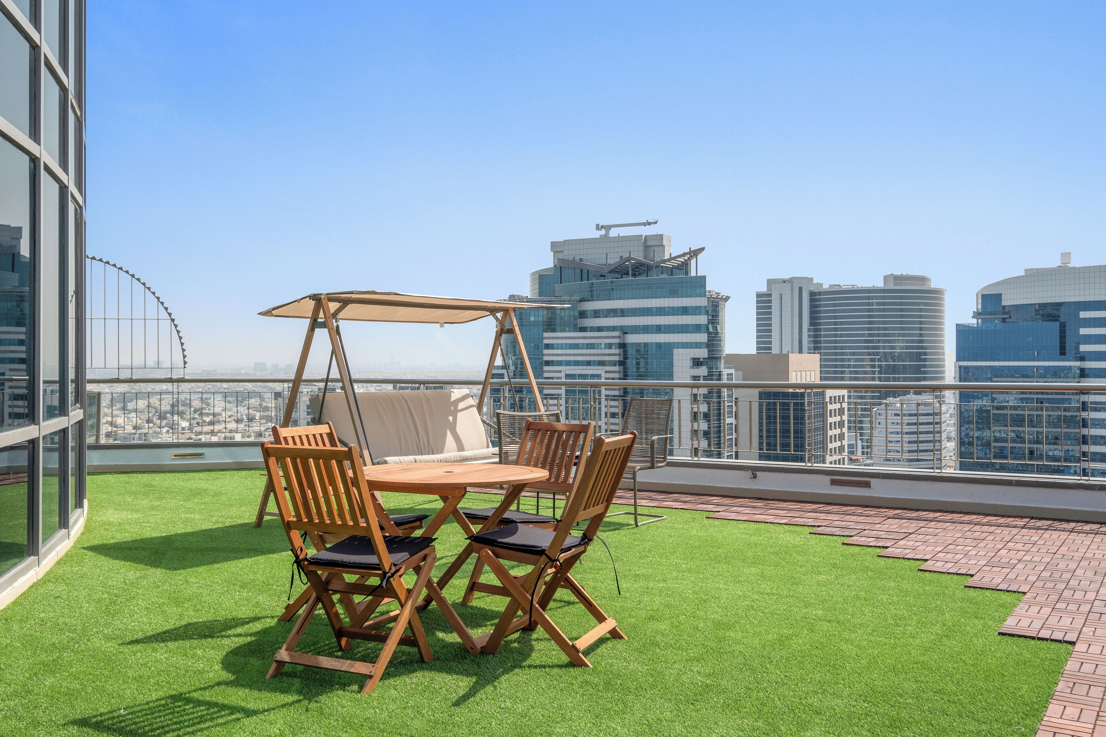 Une terrasse sur le toit, avec une balançoire, deux chaises en bois, une table et une vue sur les toits de la ville.