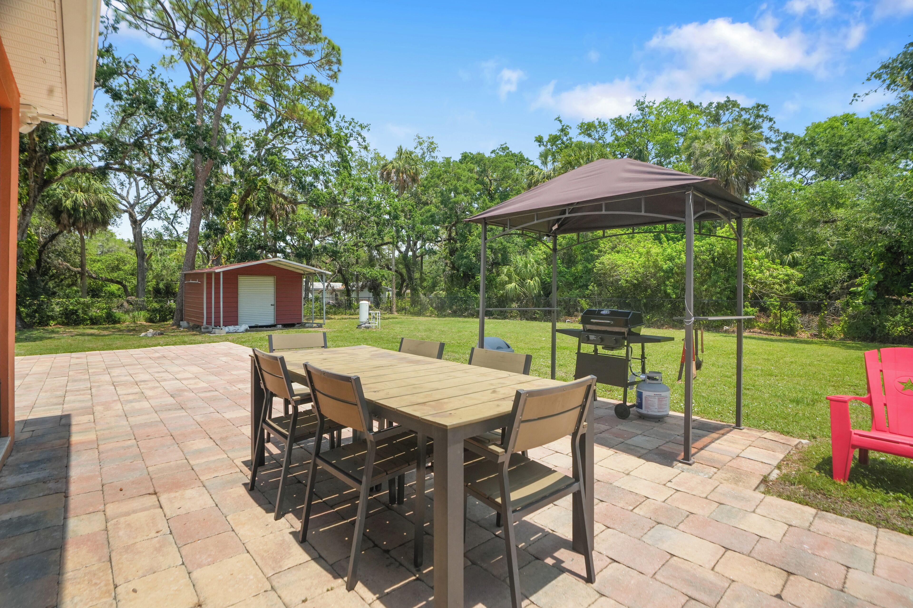 Une terrasse avec une table et des chaises en bois, un barbecue et un espace salon abrité.