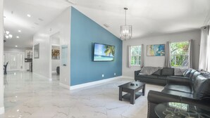 A spacious living room with a blue accent wall, a black leather sofa, a glass coffee table, and a TV mounted on the wall.