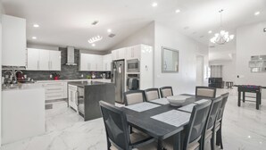 A modern kitchen with white cabinets, a central island, and a dining area with a dark table and chairs.