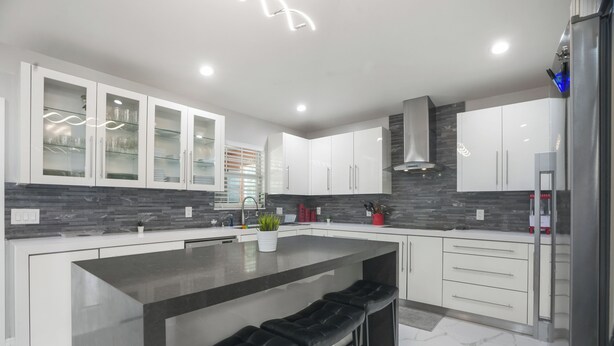 A modern kitchen with a large island, white cabinetry, and a marble backsplash.