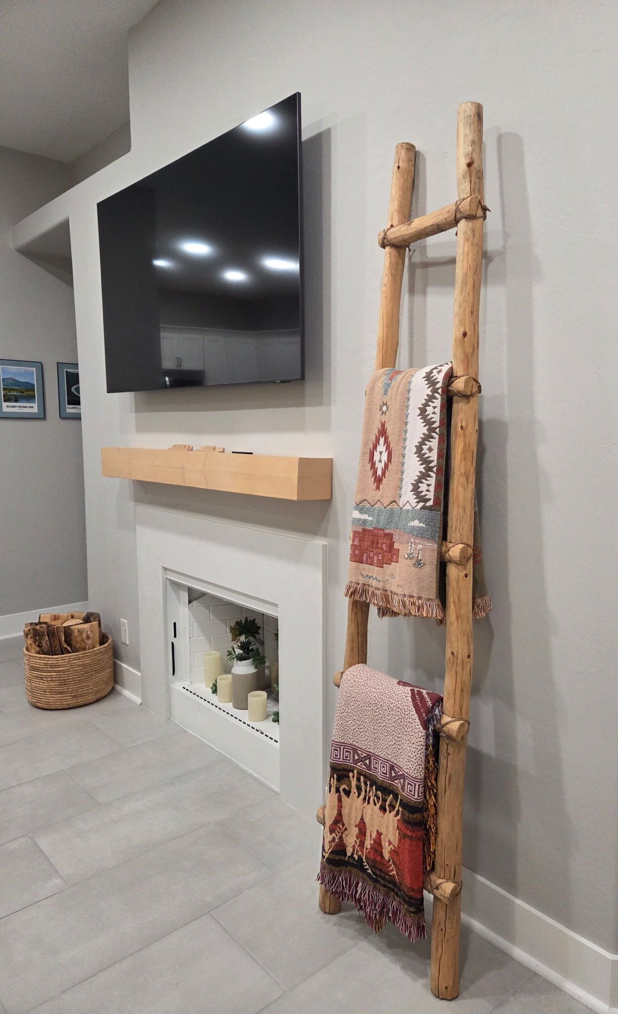 Un salon avec un téléviseur à écran plat fixé au-dessus d’une cheminée, une échelle en bois sur laquelle sont posées des couvertures et un panier en osier sur le sol.
