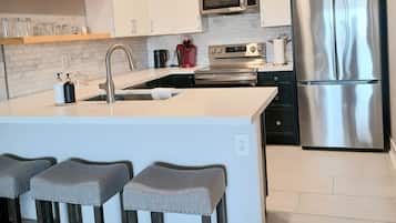 Une cuisine moderne avec des meubles blancs, des appareils en acier inoxydable et un îlot central doté de tabourets de bar.