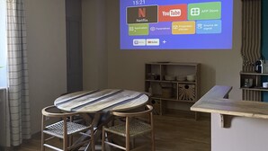 A living room with a wooden dining table, chairs, a TV mounted on the wall displaying streaming apps, and a hanging plant. - Le Cocon, L'Échiquier (Castres)