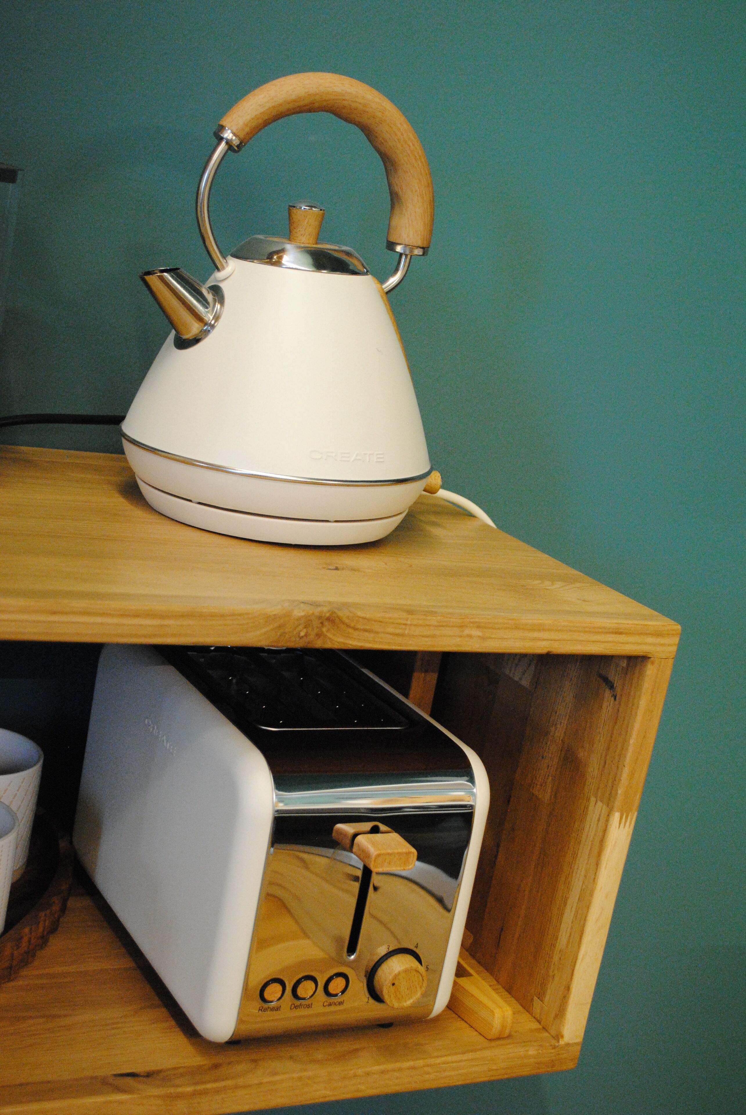 A white kettle with a wooden handle on a wooden shelf.