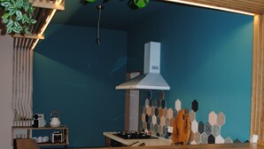 A kitchen with a blue wall, wooden stools, a hanging plant, and a white stove. - Le Cocon, L'Échiquier (Castres)