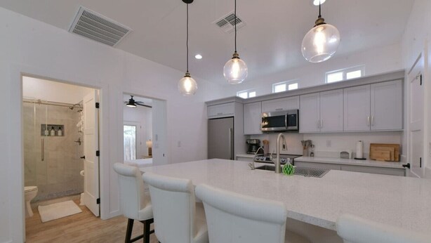 Una cocina moderna con una isla grande, armarios blancos e iluminación colgante.