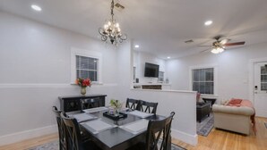Un comedor con una mesa y sillas negras, una araña y un televisor montado en la pared.
