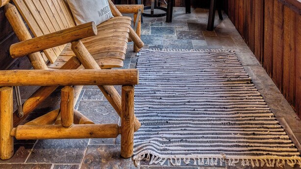 Een houten veranda met drie Adirondack-stoelen, een kleine tafel met een plant in pot, en uitzicht op bomen door grote ramen.