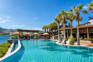 A pool with a clear blue water feature, surrounded by palm trees and a wooden deck. - Voger Bodrum By The Sea (Bodrum)