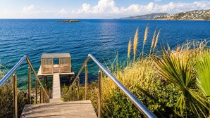 Un escalier en bois mène à une petite construction en bois située au bord de la mer, d’où l’on a une vue dégagée sur l’océan et le paysage lointain.