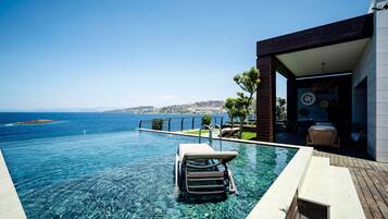 Ein Pool ohne Ende mit klarem Wasser, einer Liege und Blick auf das Meer.