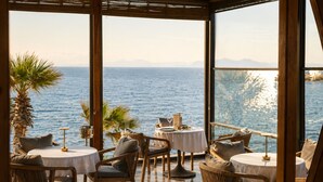 Un restaurant en bord de mer avec des tables rondes, des chaises en osier et une vue sur l’océan.