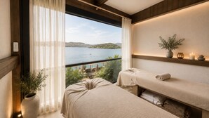 Une pièce avec un balcon, une table de massage, une étagère avec des plantes et une vue sur la mer.
