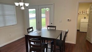 Un coin repas avec une table et des chaises en bois foncé, un lustre et une vue sur l’extérieur, accessible par une porte vitrée.