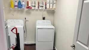 Une buanderie équipée de deux machines à laver, d’un sèche-linge et d’une étagère contenant des produits de nettoyage.