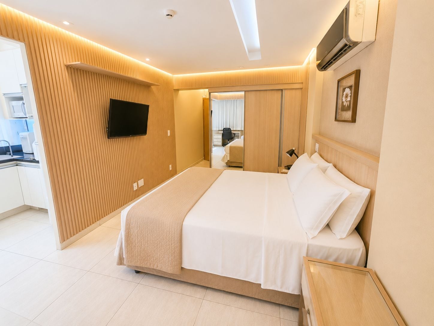 A modern hotel room with a large bed, a flat-screen TV mounted on the wall, and a view into the adjacent bathroom.