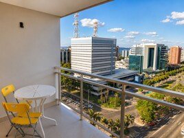 Un balcón con vista a un paisaje urbano, una mesa con sillas y una ventana con persianas.
