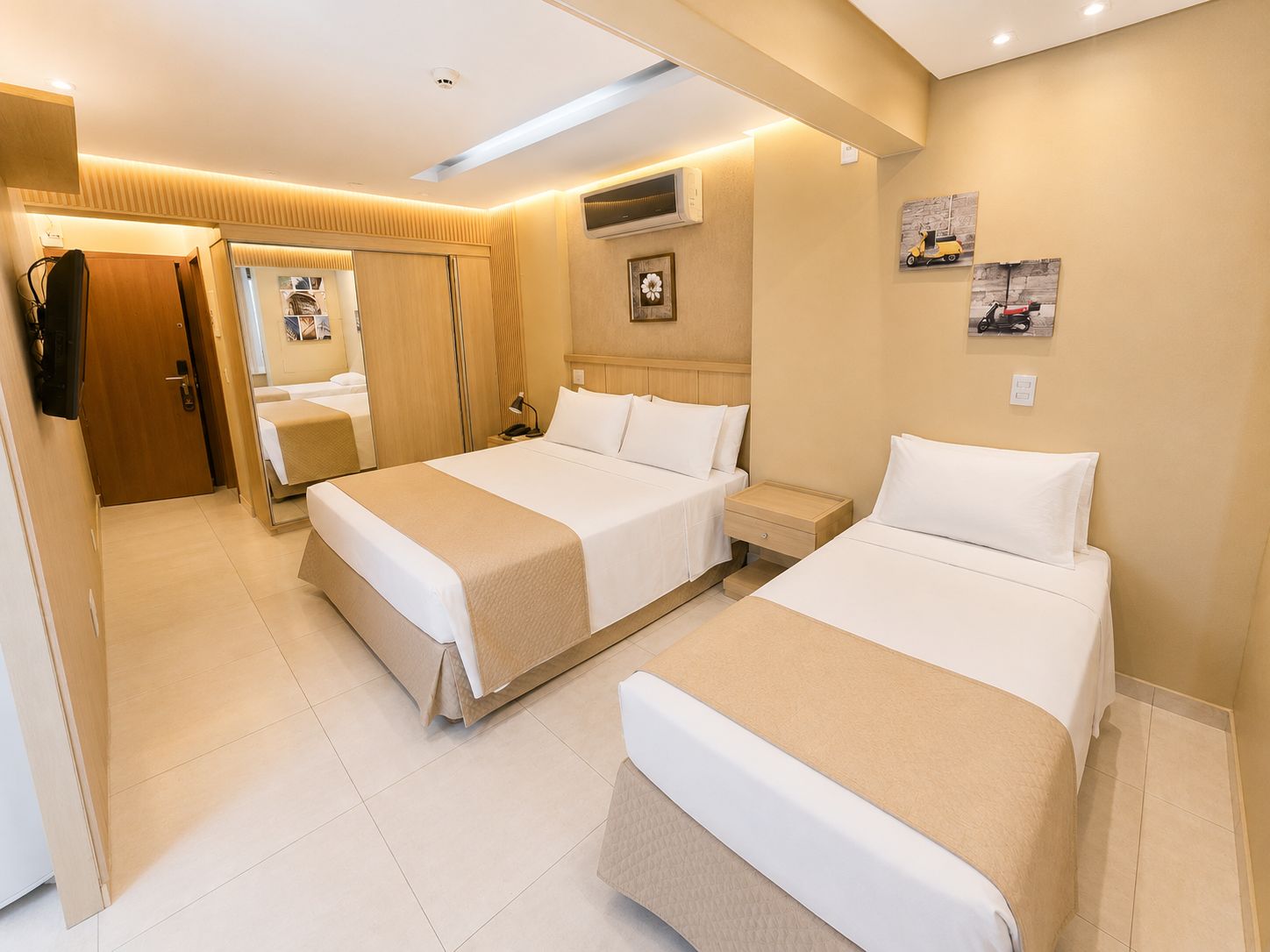 Habitación de hotel con dos camas, un armario, un espejo y una mesita.