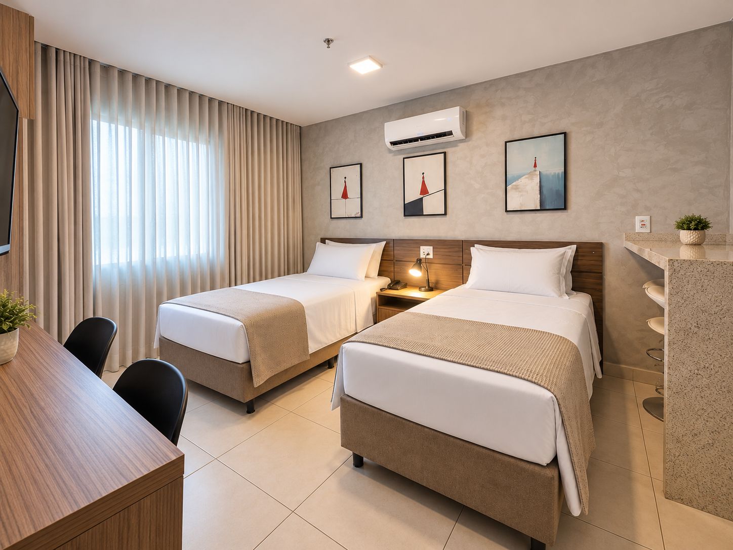 A hotel room with two beds, a desk, and a small kitchenette.