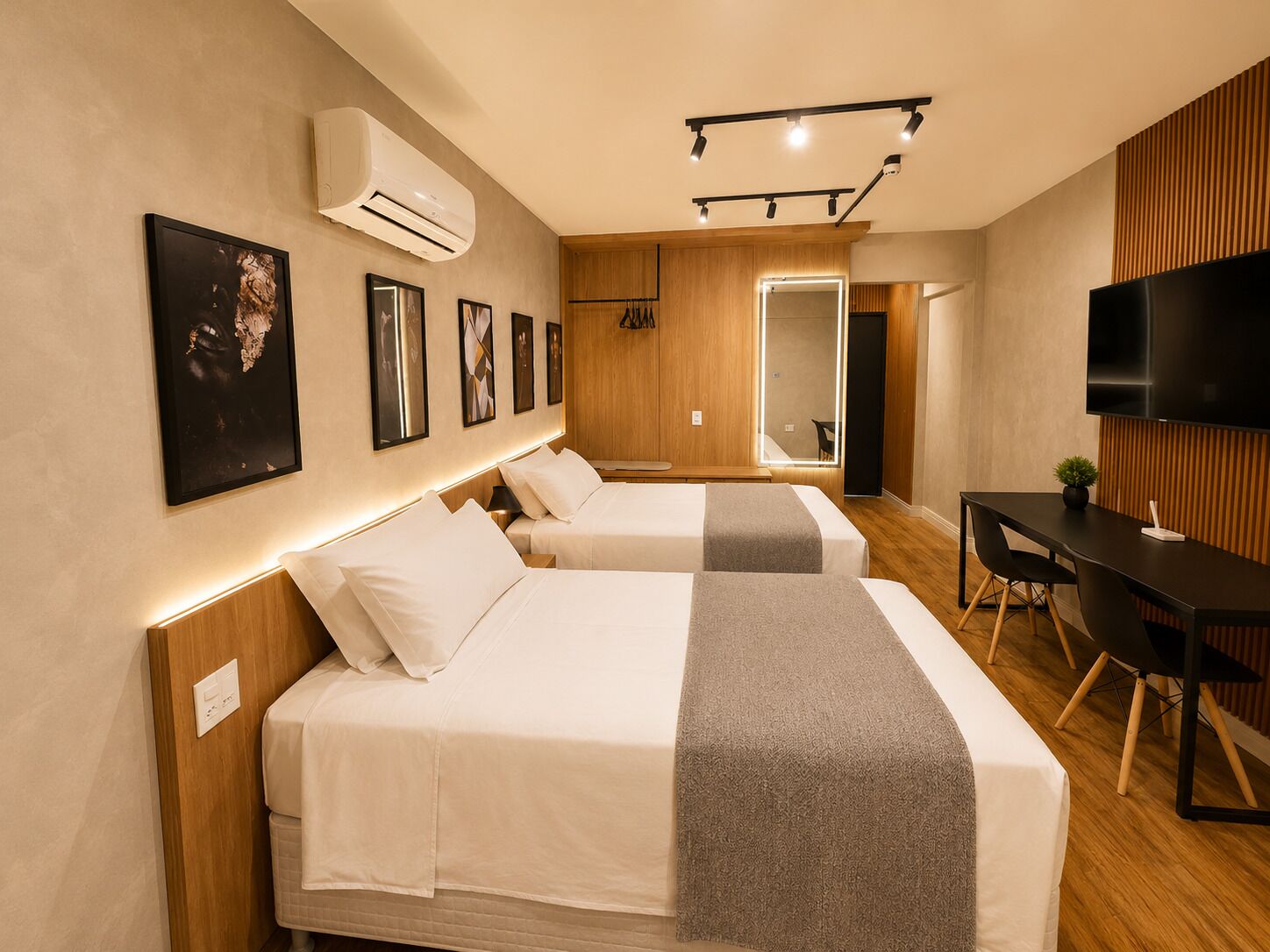 A hotel room with two beds, a desk, a TV, and a mirror.