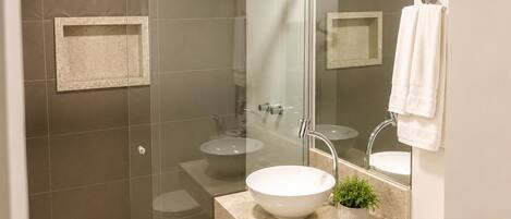 A modern bathroom with a glass shower enclosure, a freestanding sink, and a toilet.