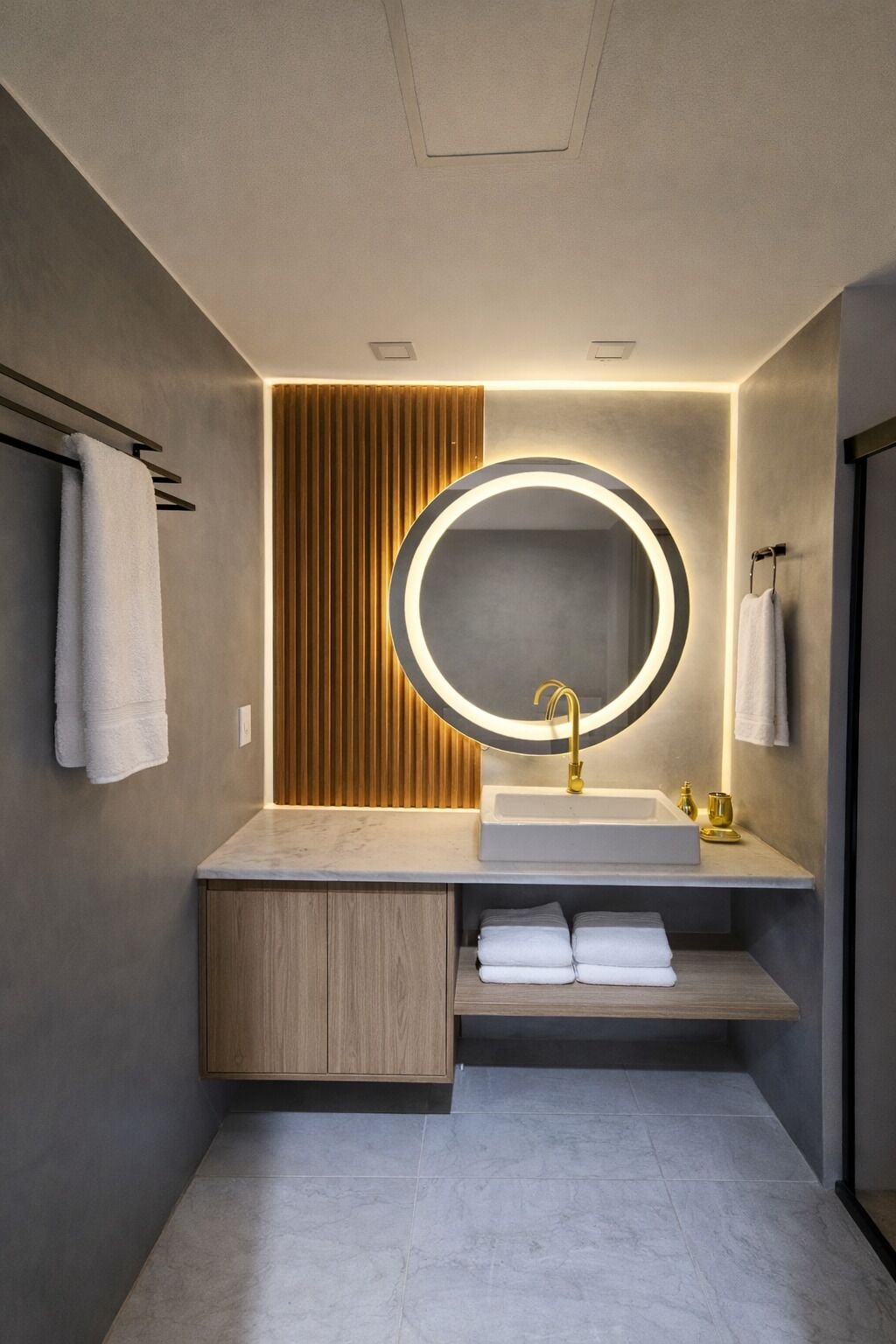 Een moderne badkamer met een ronde spiegel, een gouden kraan en een wandpaneel van hout.