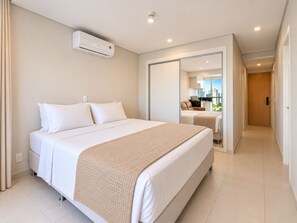 Une chambre d’hôtel avec un grand lit, un climatiseur placé près du lit et une vue sur la ville, visible à travers une porte vitrée.